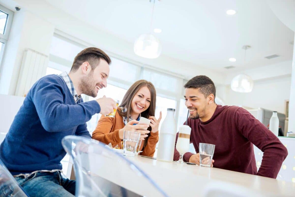 Three people sit at an office kitchen drinking water and coffee made from instantly purified hot water tap. 