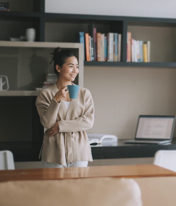 Asian woman holding a cup of coffee in her home office.