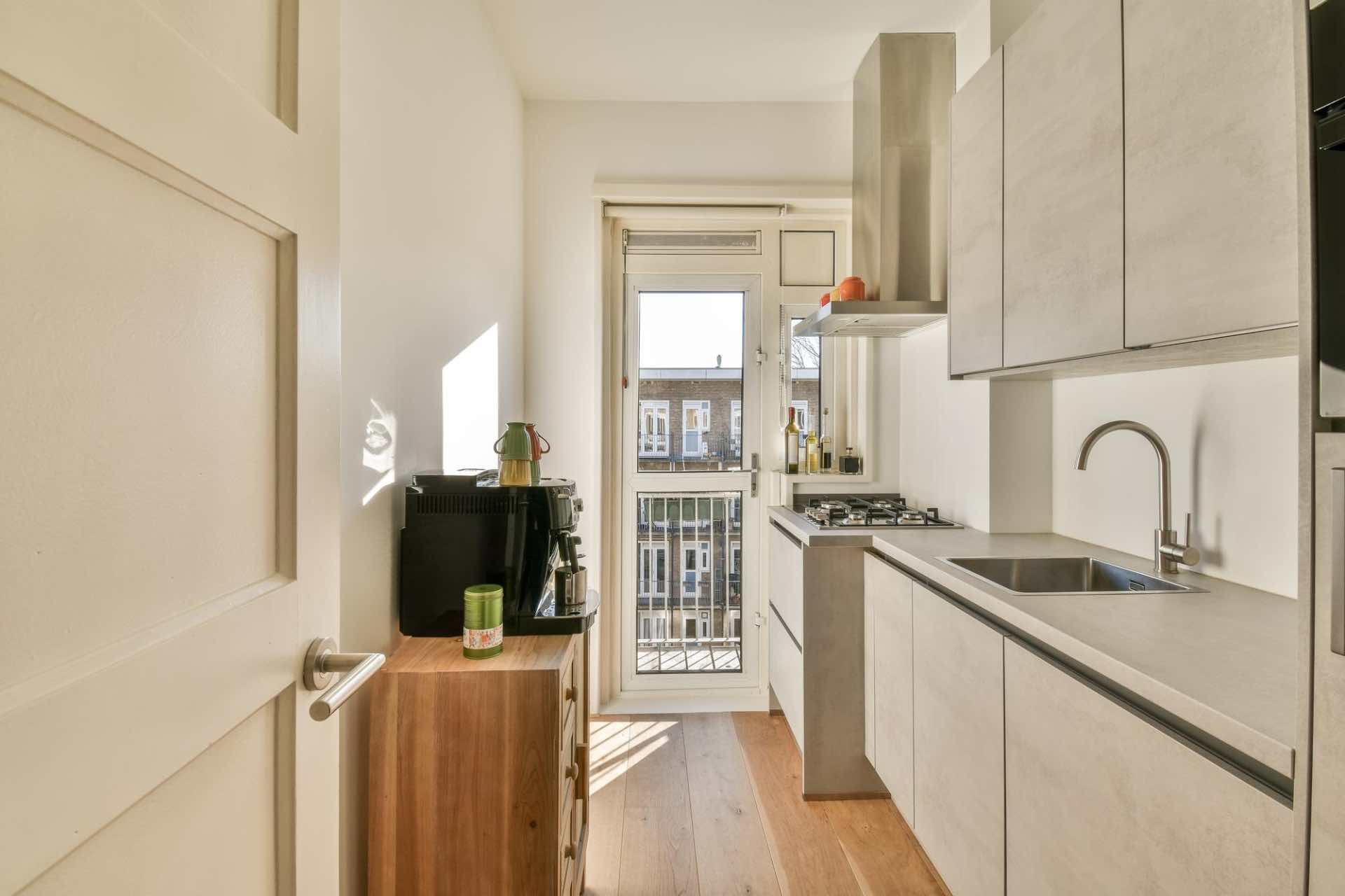 A narrow, modern kitchen with light cabinets, a gas stove, sink, coffee machine, and water purifying system installed
