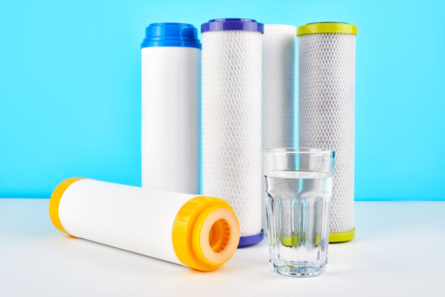 Water filter cartridges and a glass of water on a blue background.